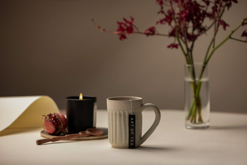 A cup of tea using an Art of Tea teabag sitting next to a lit candle and bouquet of flowers